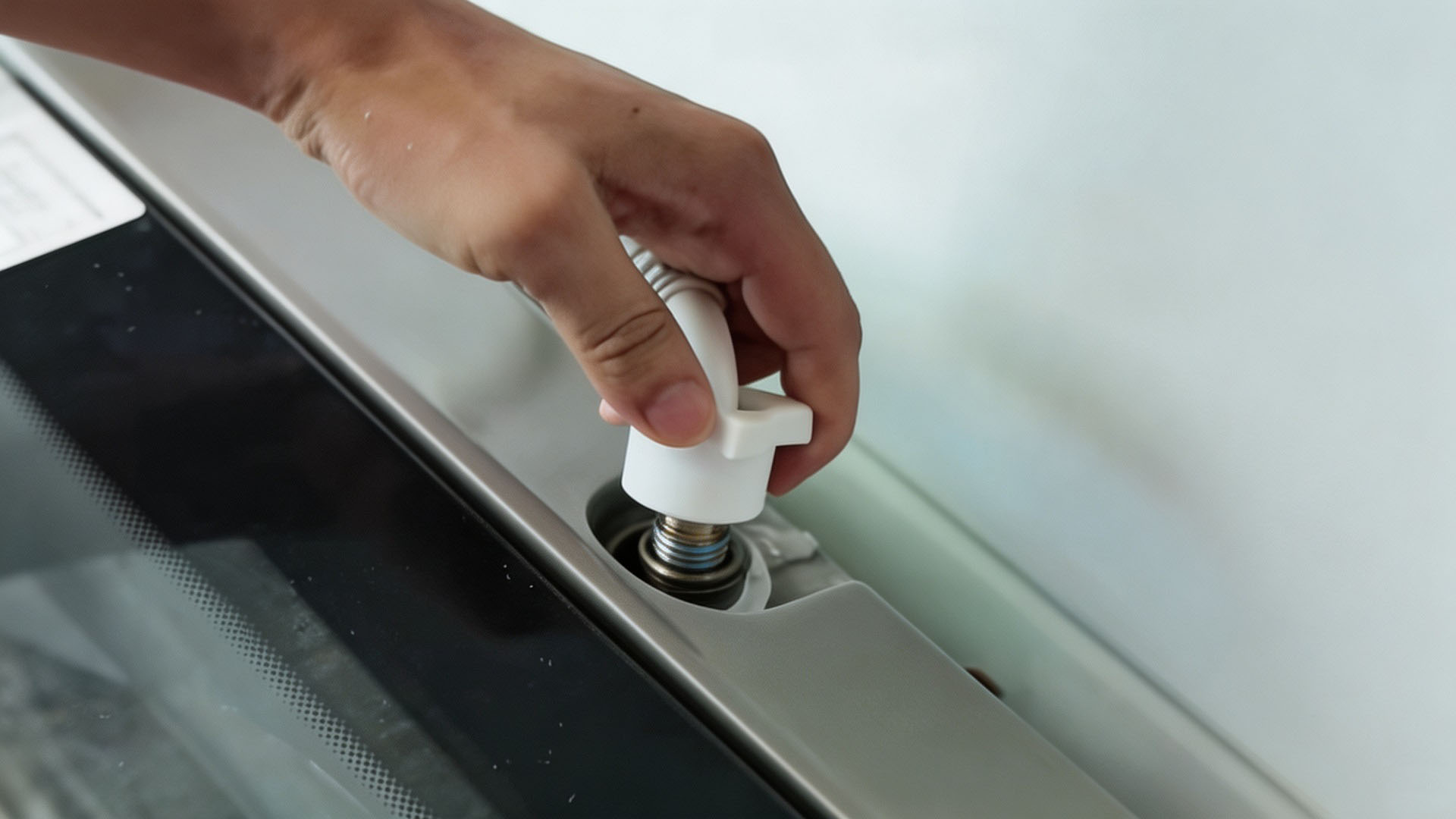 A hand loosens the washing machine inlet hose connecting nut counterclockwise.