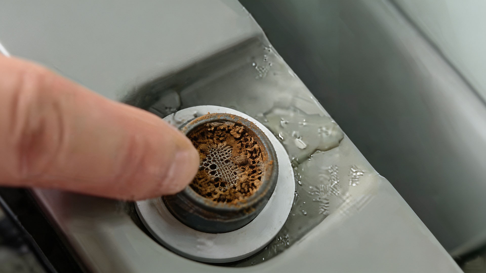 Close-up of a washing machine inlet filter screen heavily clogged with brown sediment, rust and limescale.