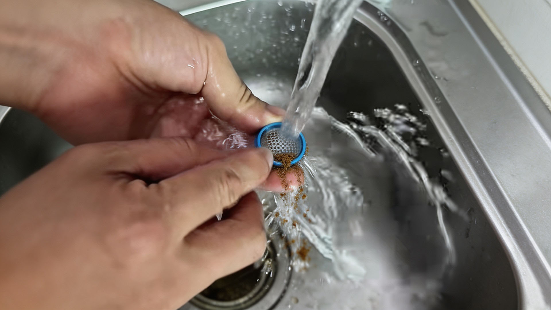 A person holds a removed washing machine filter screen under running tap water to rinse away dirt and limescale.